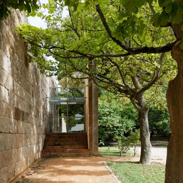 Entrada da Casa das Artes pelo jardim, muro de pedra e árvores