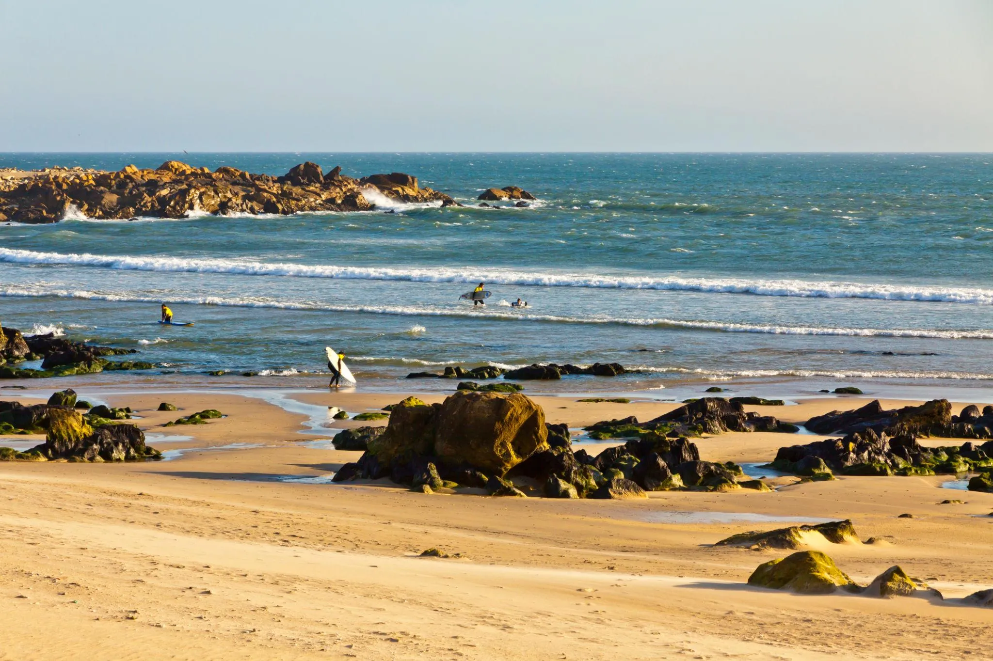Praia rochosa de Matosinhos com surfistas ao fundo