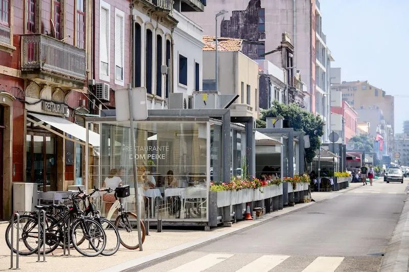 Rua de restaurantes de peixe em Matosinhos, com bicicletas e marquises de vidro