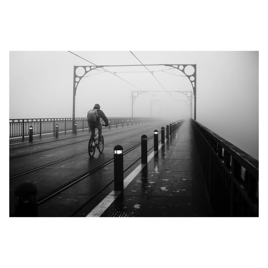 Ciclista a atravessar a Ponte D. Luís I no nevoeiro da manhã