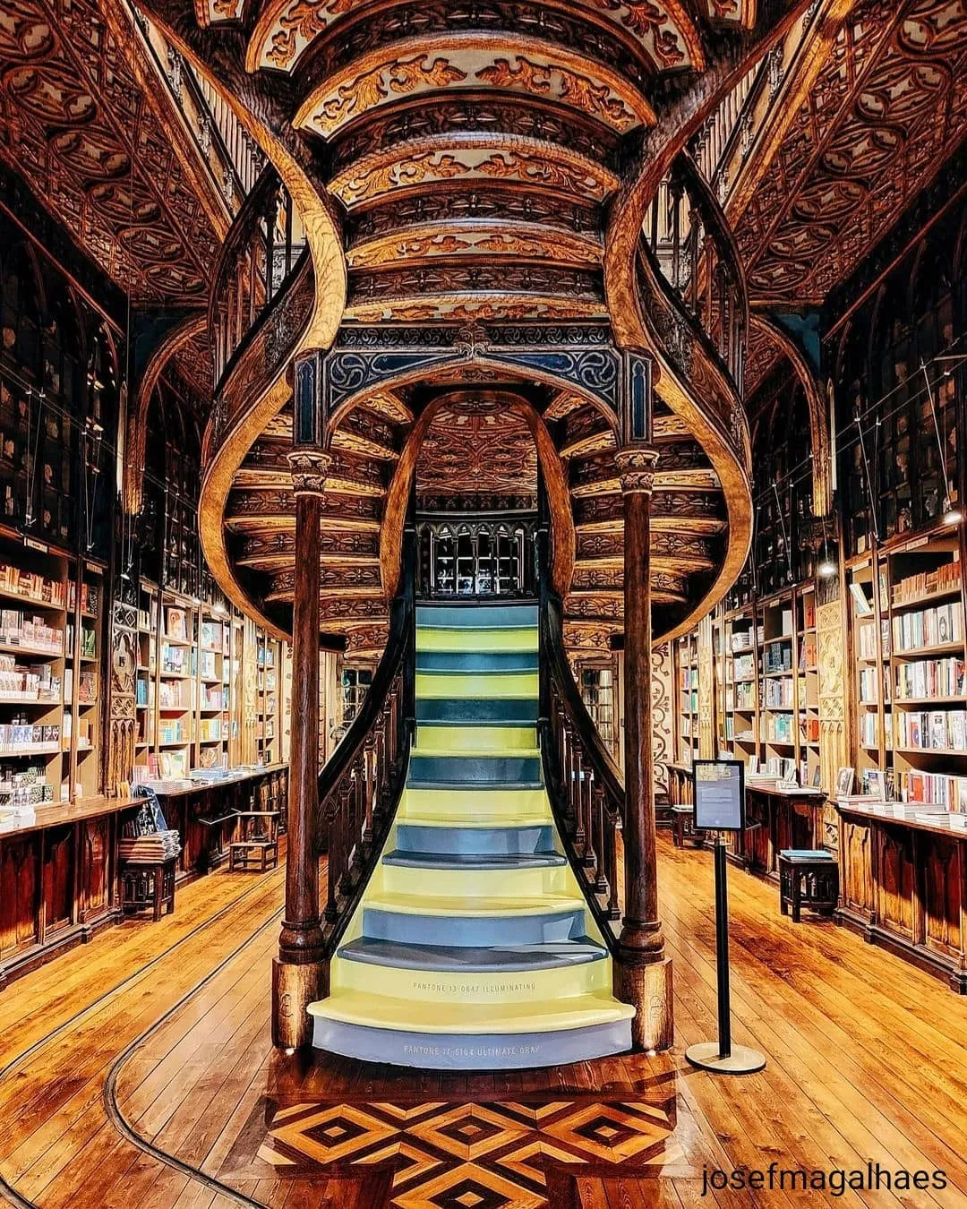 Escadaria de madeira da Livraria Lello vista de baixo, com tons amarelos e azuis