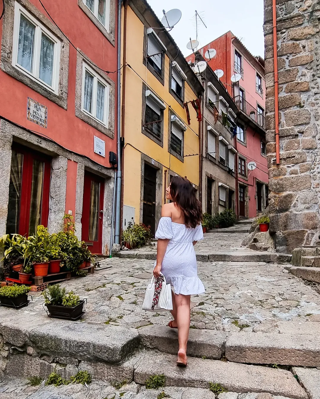 Mulher a subir a Rua da Pena Ventosa com casas coloridas dos dois lados