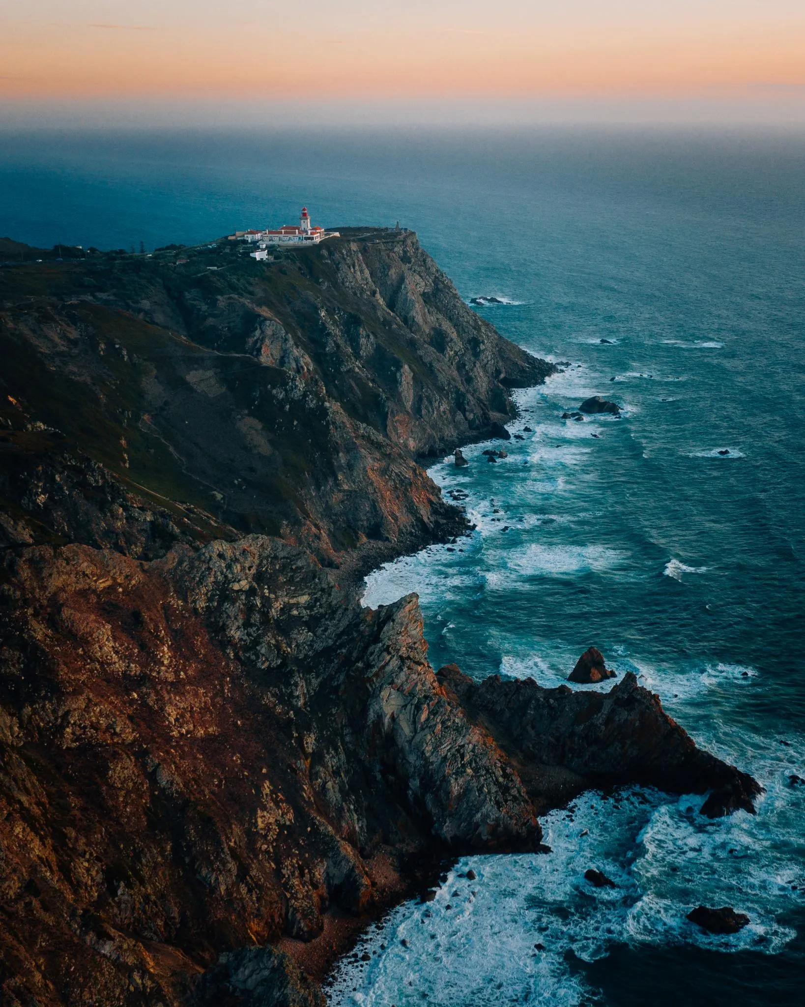 Cabo da Roca ao pôr-do-sol, com farol e arribas a cair sobre o Atlântico